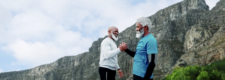 Older mens clasp hands by a mountain.